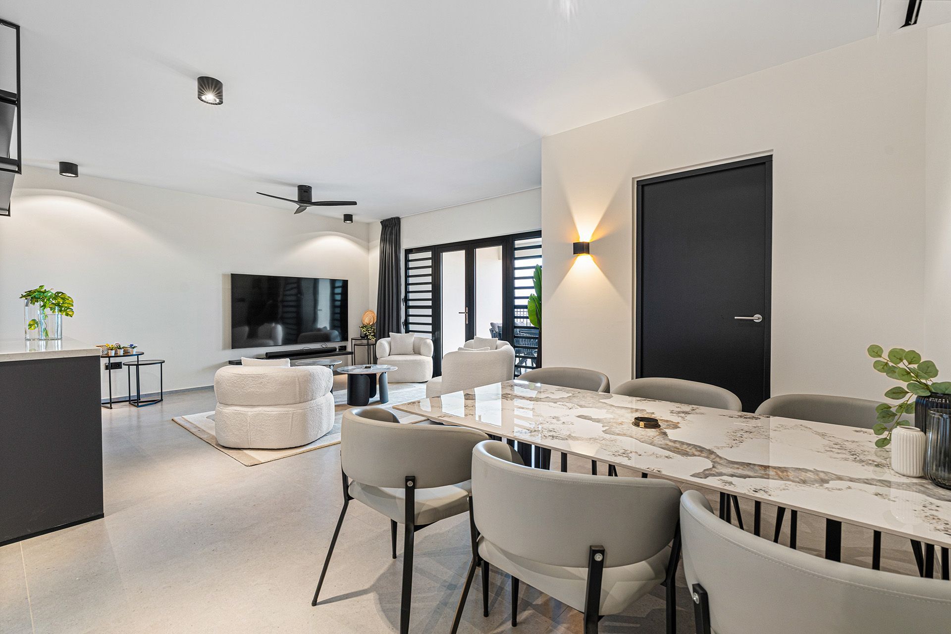 Modern living room with dining area, white walls, black door, and marble table.