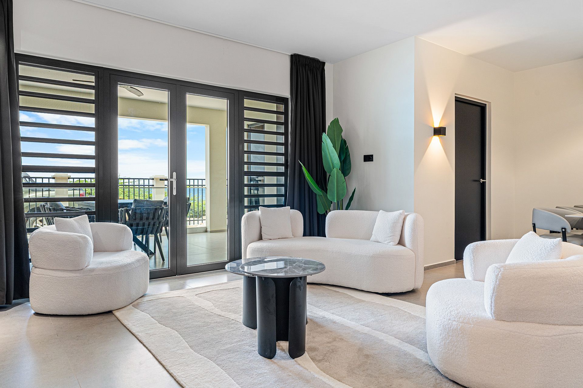 Modern living room with white sofas, black accents, and a balcony view of the ocean.