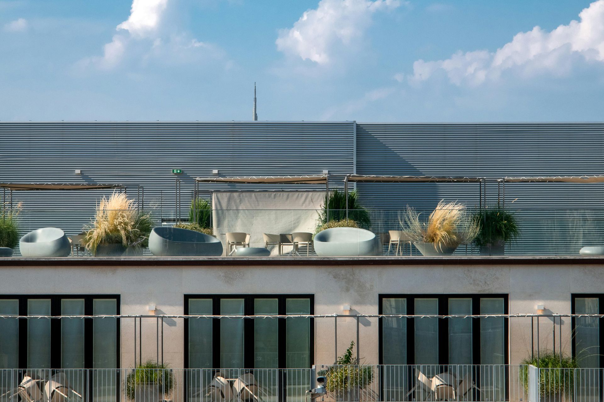 Rooftop patio with seating and plants atop a building with many windows, against a blue sky.