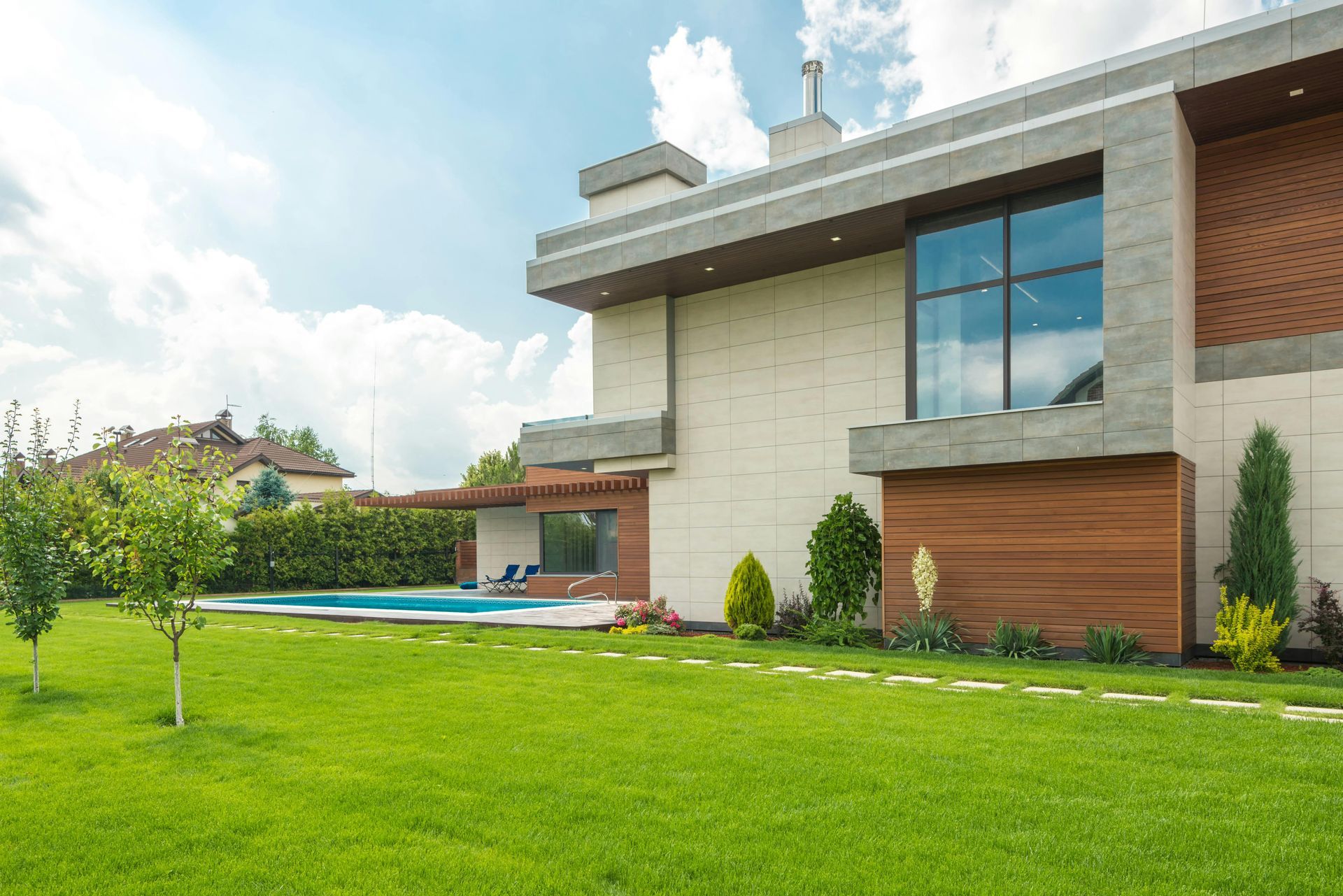 Modern house with pool, lush green lawn, bright blue sky, and sunny day.
