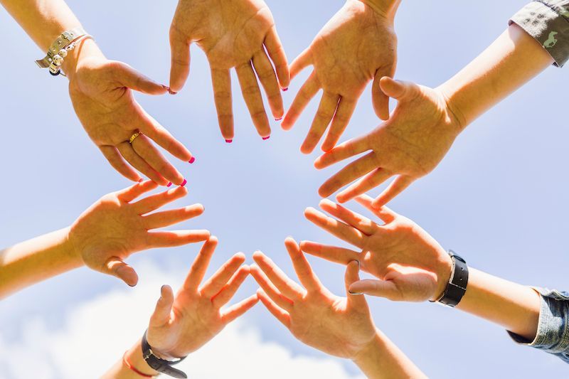 People putting their hands together in front of a blue sky background.