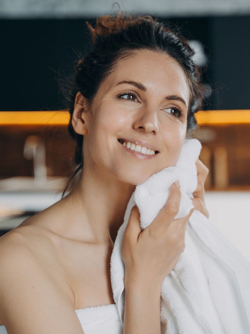 a woman is wrapped in a towel and smiling while cleaning her face with a towel .