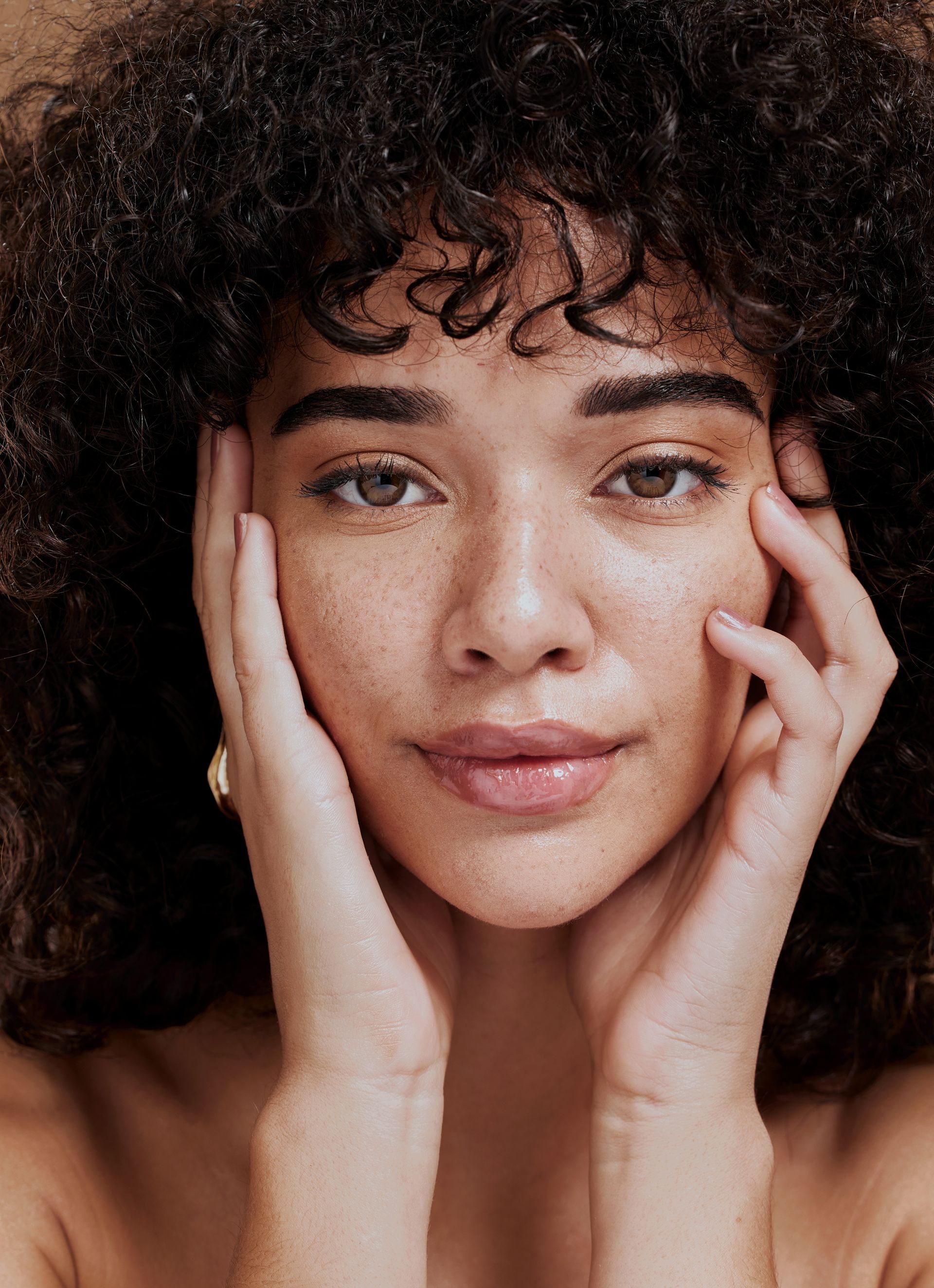a woman with curly hair and freckles is touching her face with her hands .