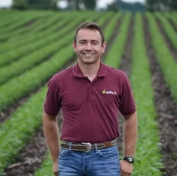 Man in burgundy polo shirt stands in field of green crops.