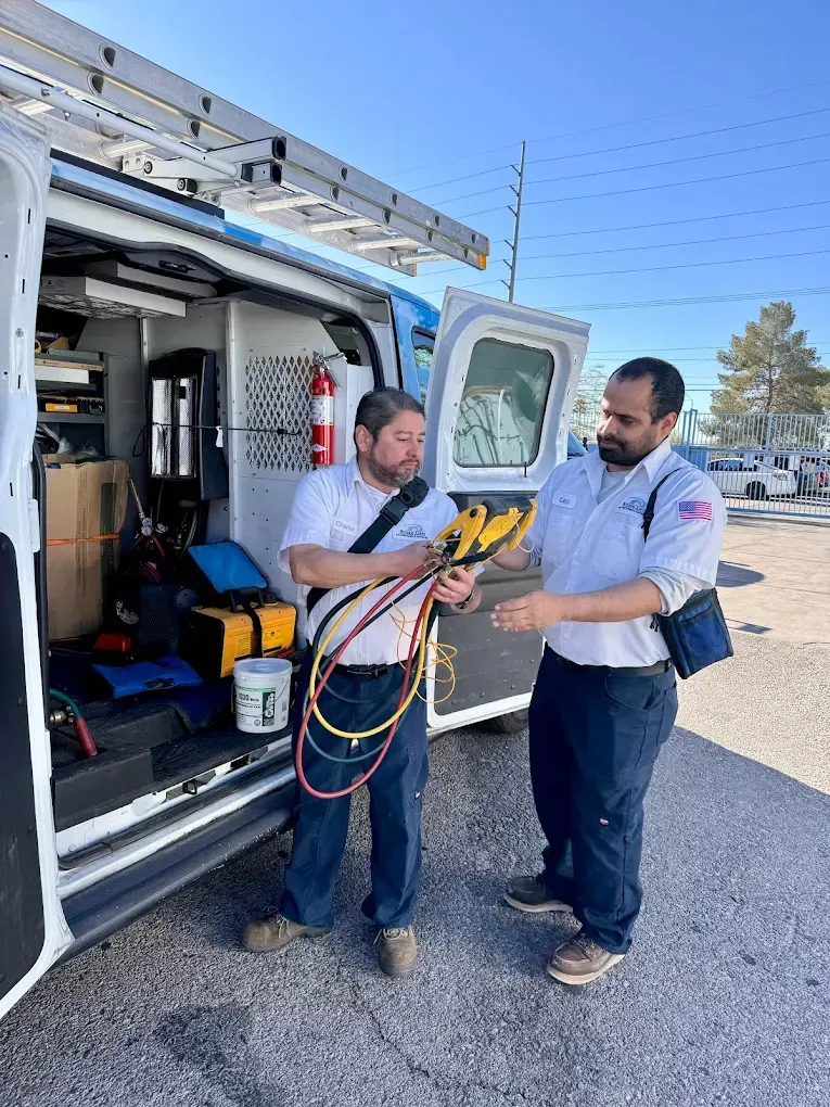 Two HVAC technicians by a service van examining gauges in daylight.