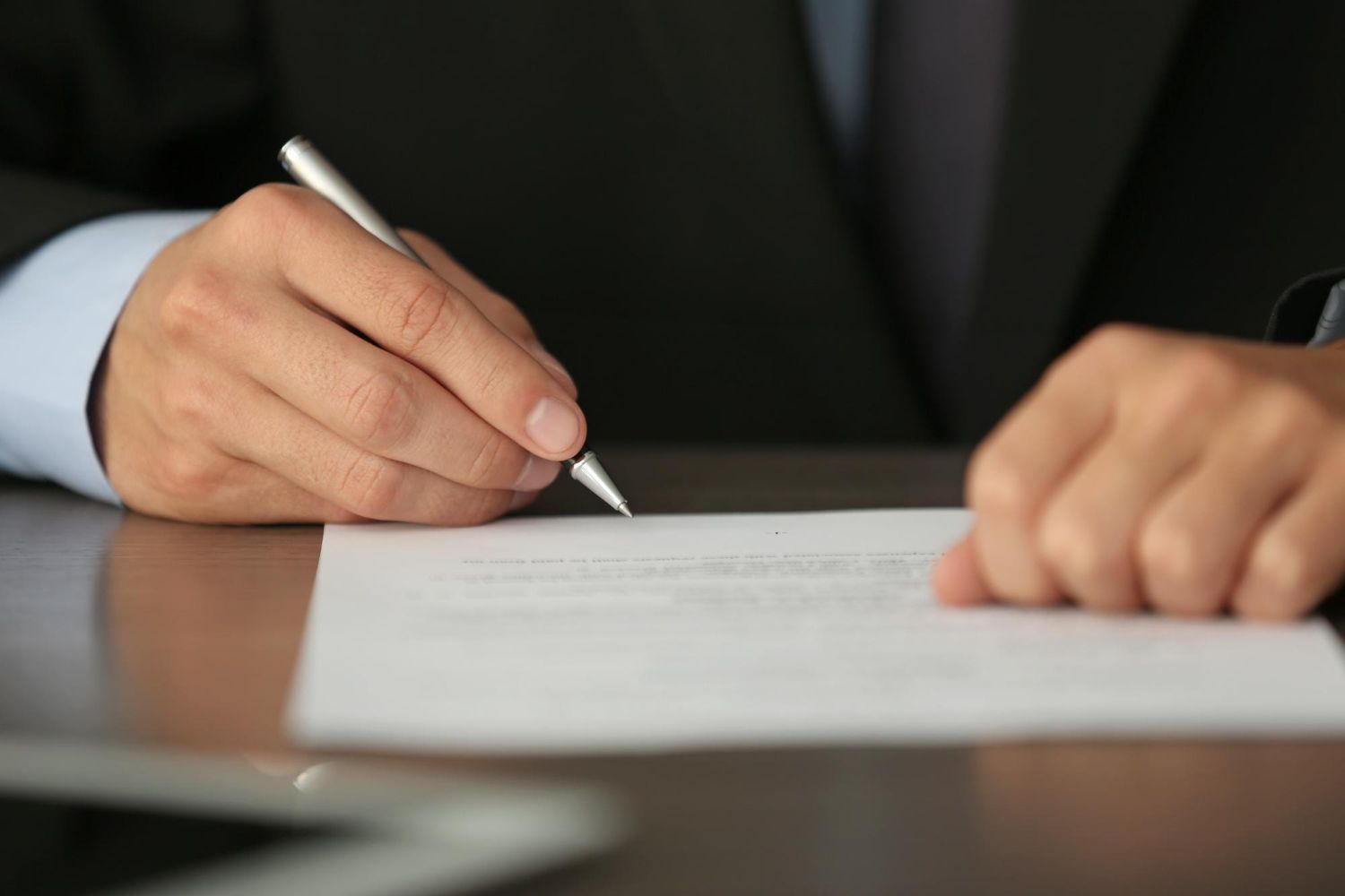 An elderly couple examines paperwork together at a table, one pointing while the other types on a laptop.