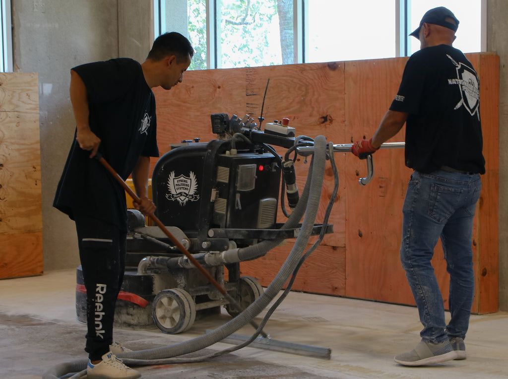 An epoxy resin flooring contractor operating a heavy-duty diamond-tipped concrete floor grinder.