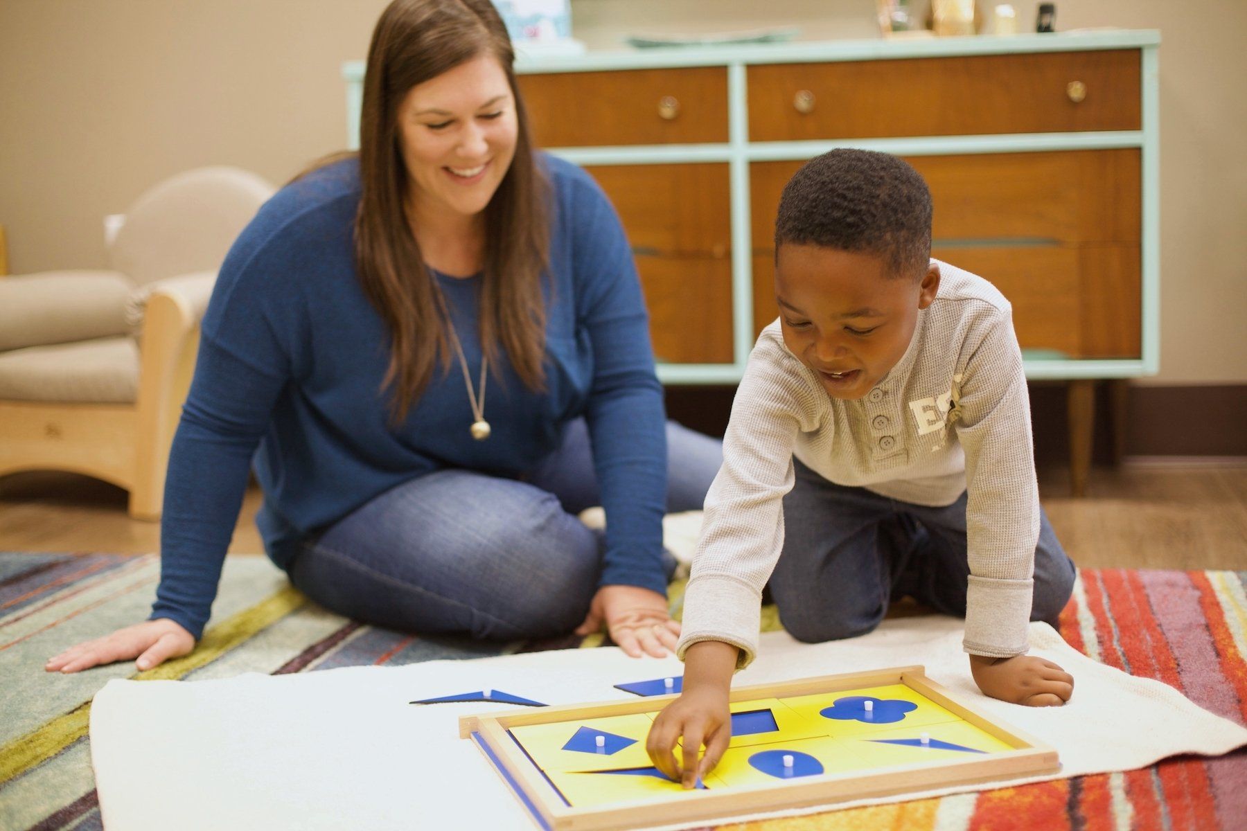 a Guide and a Montessori child are playing with a puzzle on the floor