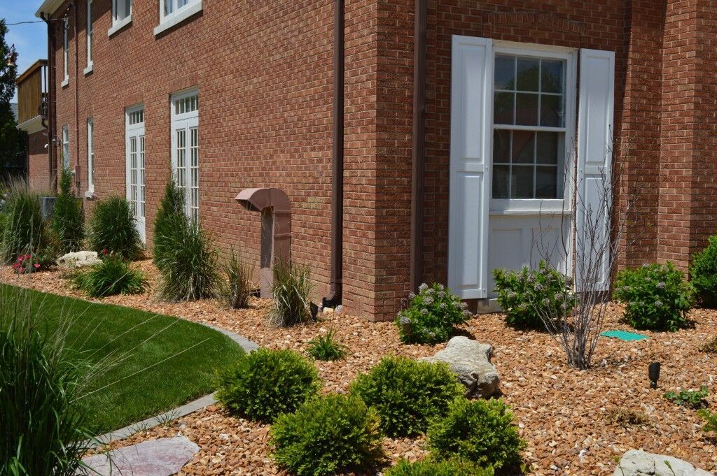 A brick house with white shutters and a lush green lawn in front of it.