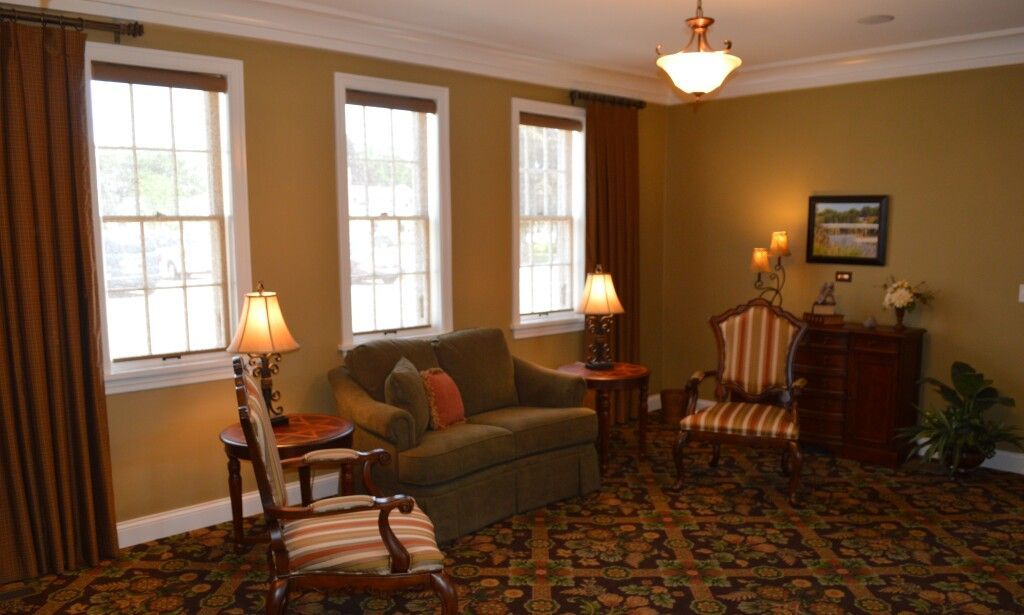 A living room with a couch , chairs , lamps and windows.