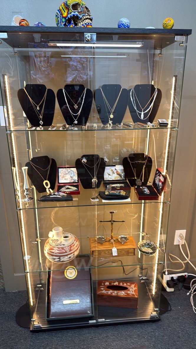A tall glass display case containing jewelry, religious items, and miscellaneous decorative objects on four shelves.