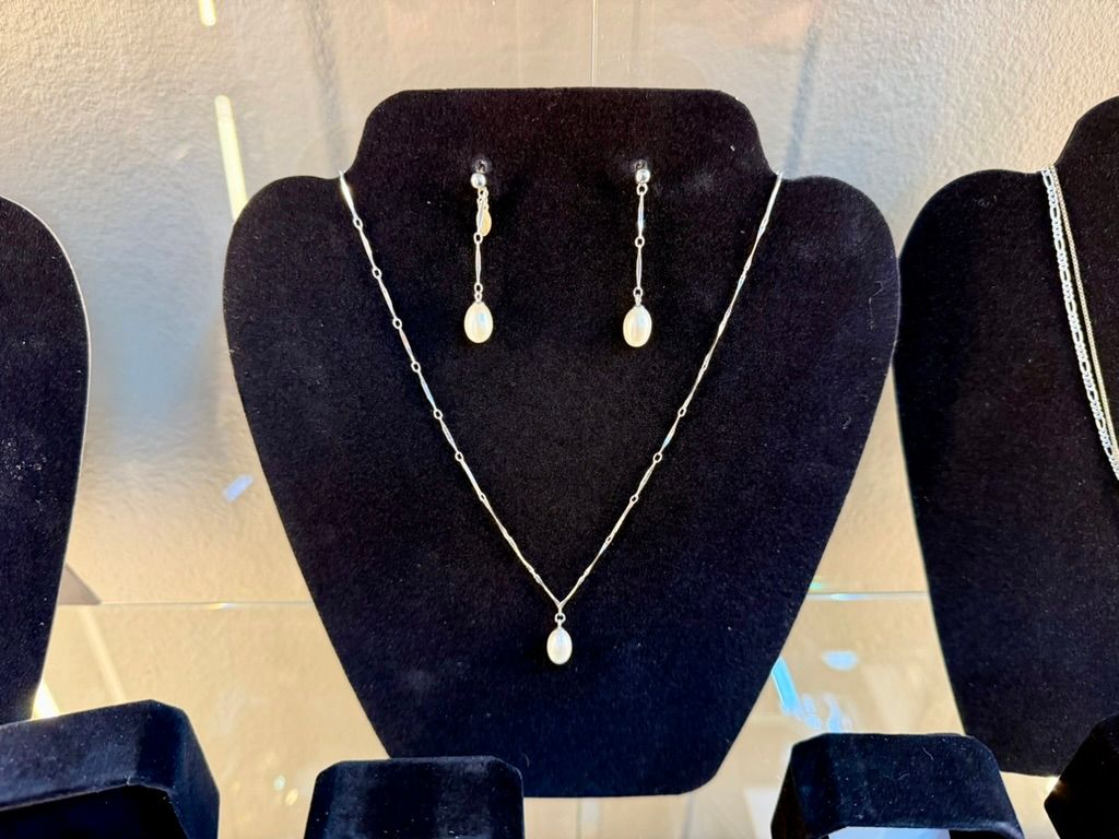 A silver necklace and matching drop earrings with small, light-colored stones displayed on a black jewelry bust.