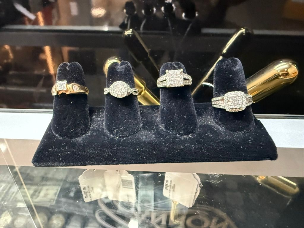 Four diamond rings displayed on a black velvet stand inside a jewelry store display case.