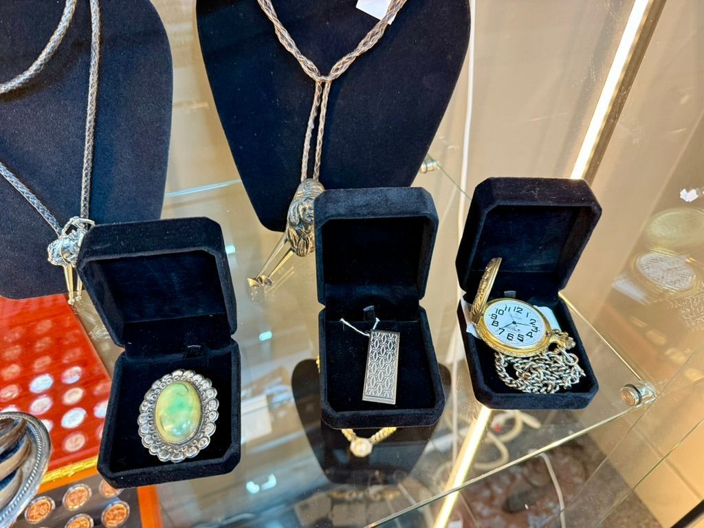 A display case holding jewelry boxes containing an opal brooch, a rectangular pendant, and a gold pocket watch.
