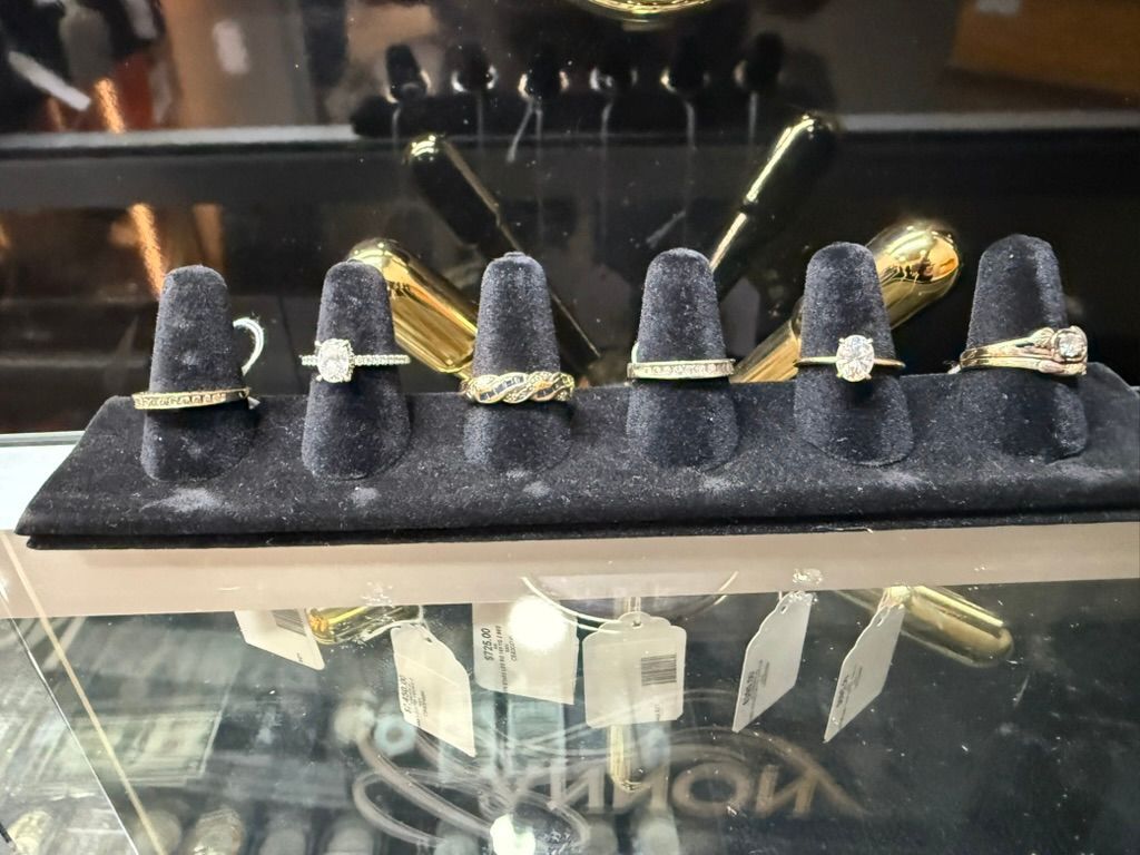 Six gold rings displayed on velvet finger stands inside a jewelry store glass case.