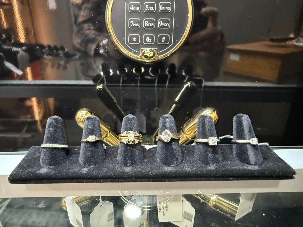 Six gold and diamond rings displayed on a black velvet stand inside a jewelry store showcase.
