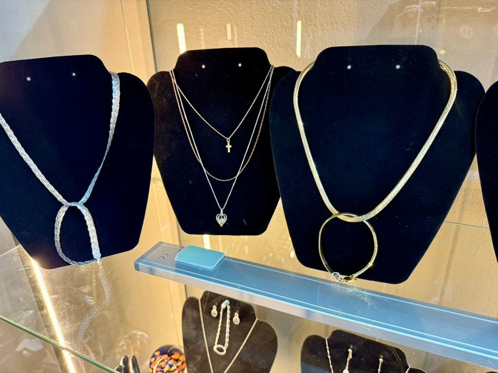 Three gold necklaces displayed on black velvet busts inside a glass retail store display case.
