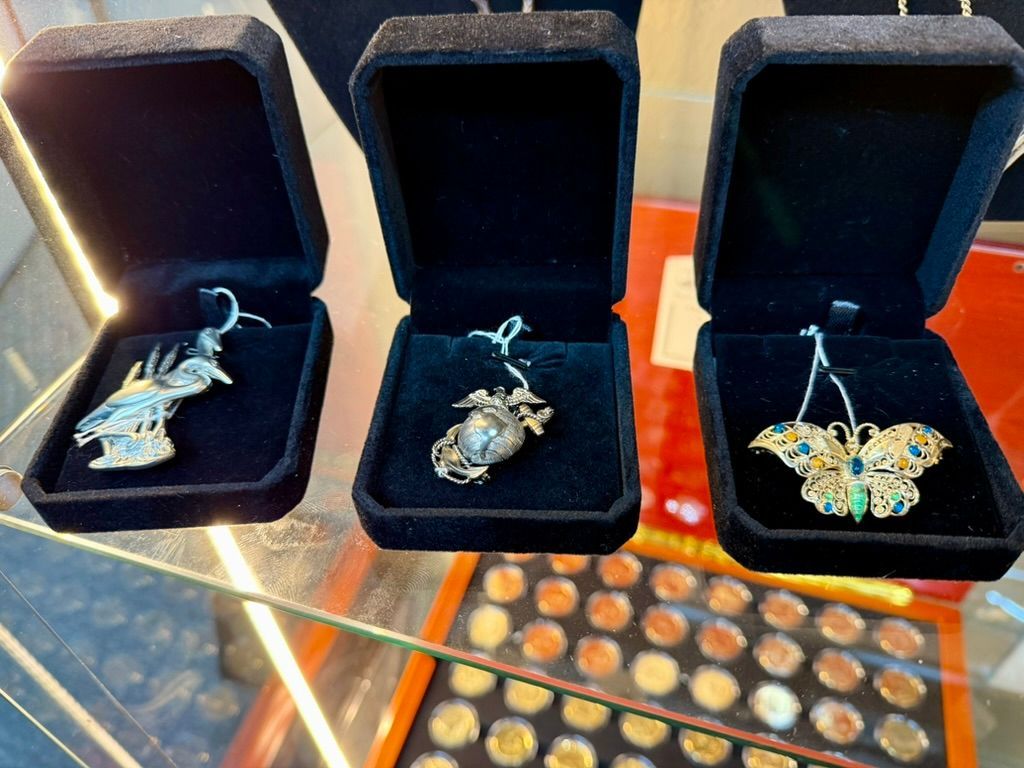 Three vintage brooches in black velvet jewelry boxes displayed on a glass shelf above a collection of small round coins.