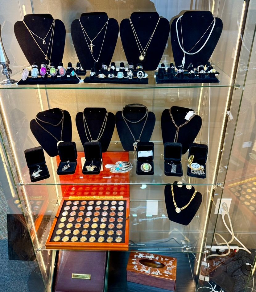 A glass display case filled with jewelry, including necklaces on mannequins, rings, a coin collection, and small boxes.