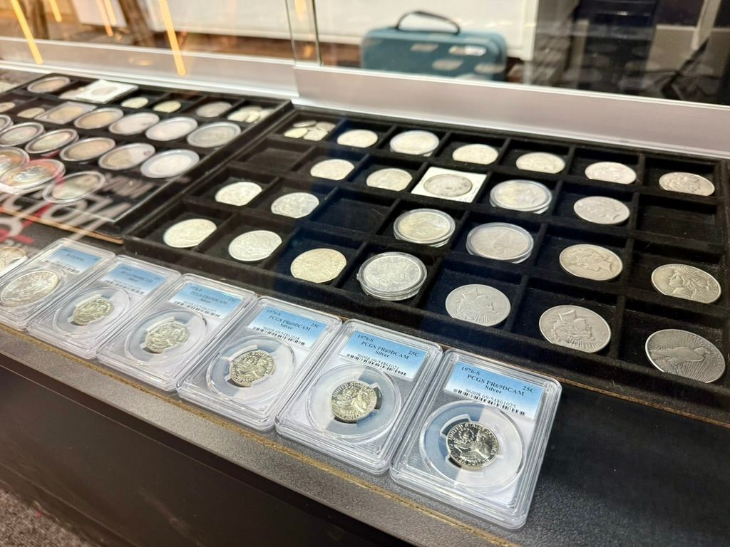 A display case filled with rows of round silver coins in a black tray, with several coins encapsulated in plastic slabs.