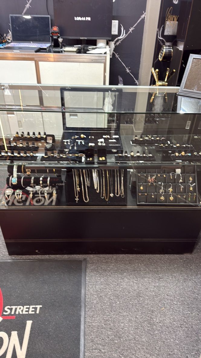 A glass jewelry display case in a retail store, filled with various rings, necklaces, and other accessories on black stands.