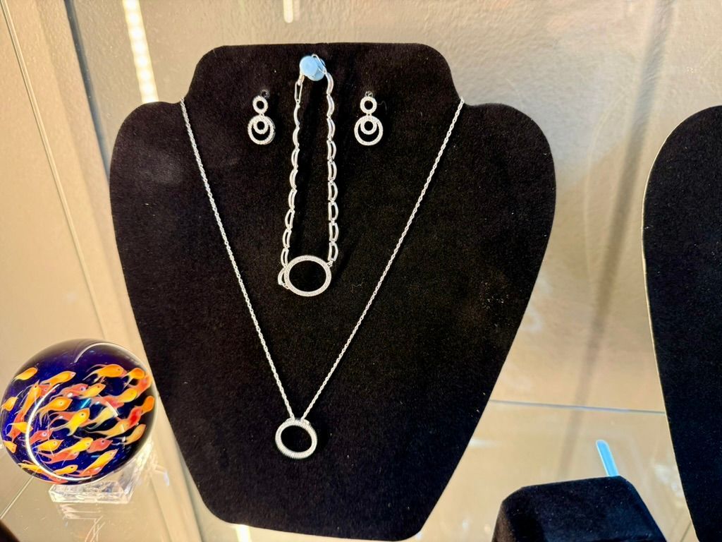 A black jewelry display stand featuring a matching necklace, bracelet, and drop earrings with circular diamond accents.