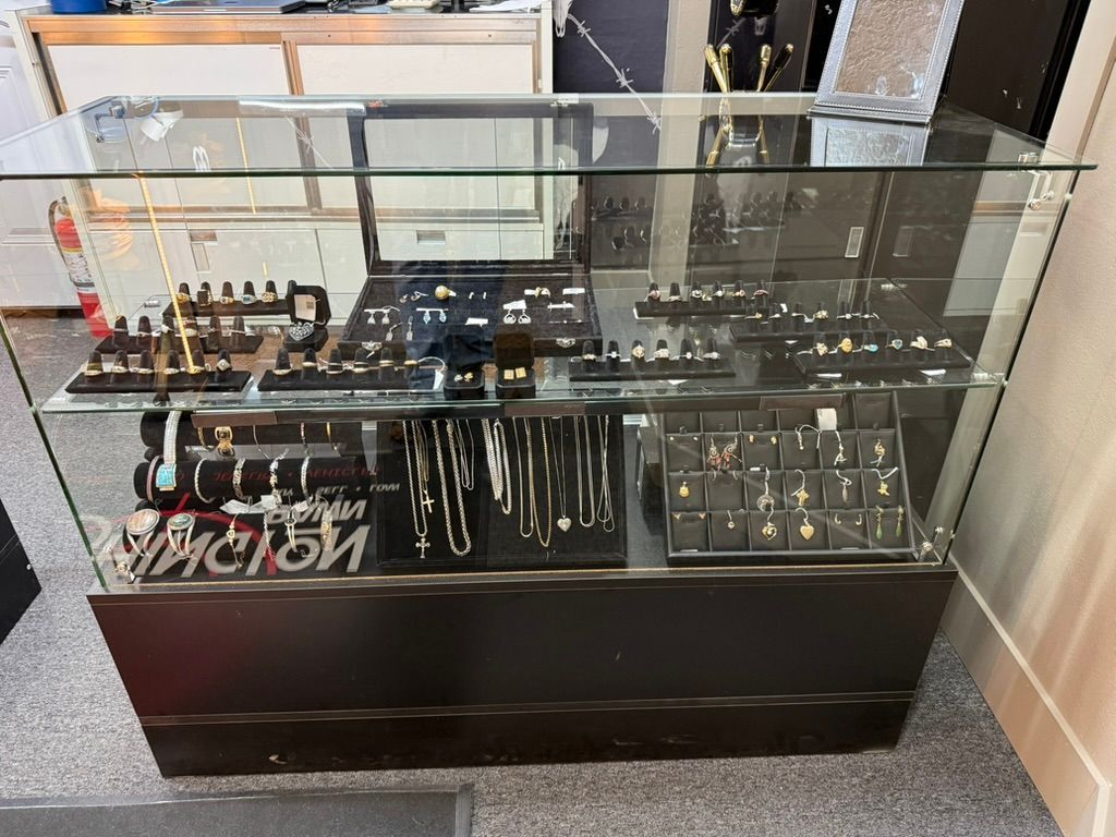 A glass display case in a store, filled with various gold and silver necklaces, rings, and jewelry sets on black stands.
