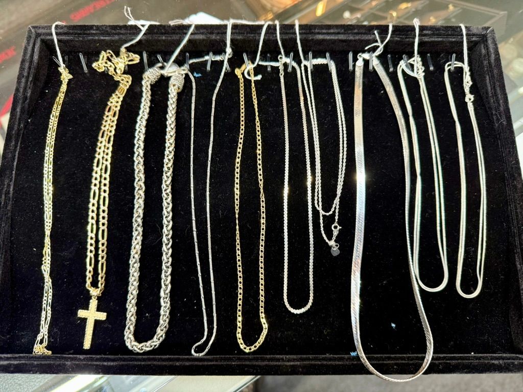A black jewelry display tray holds ten various silver and gold chains, including one with a cross pendant.