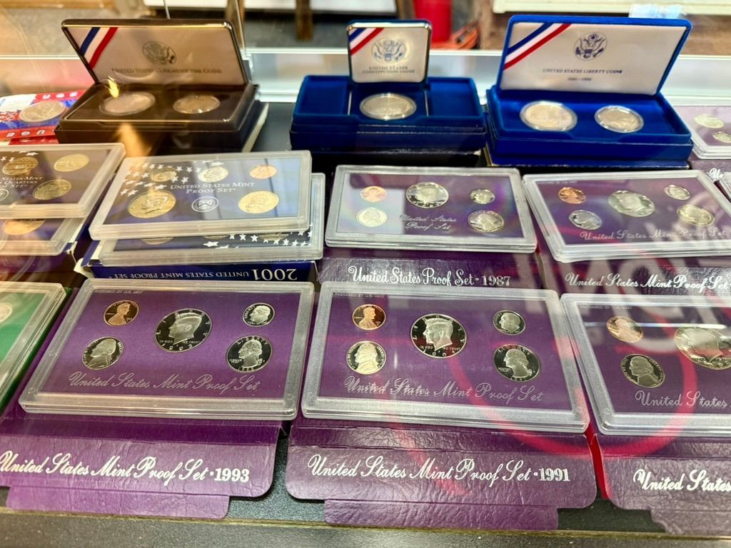 Several United States Mint proof coin sets and individual commemorative coins displayed in their cases on a shelf.