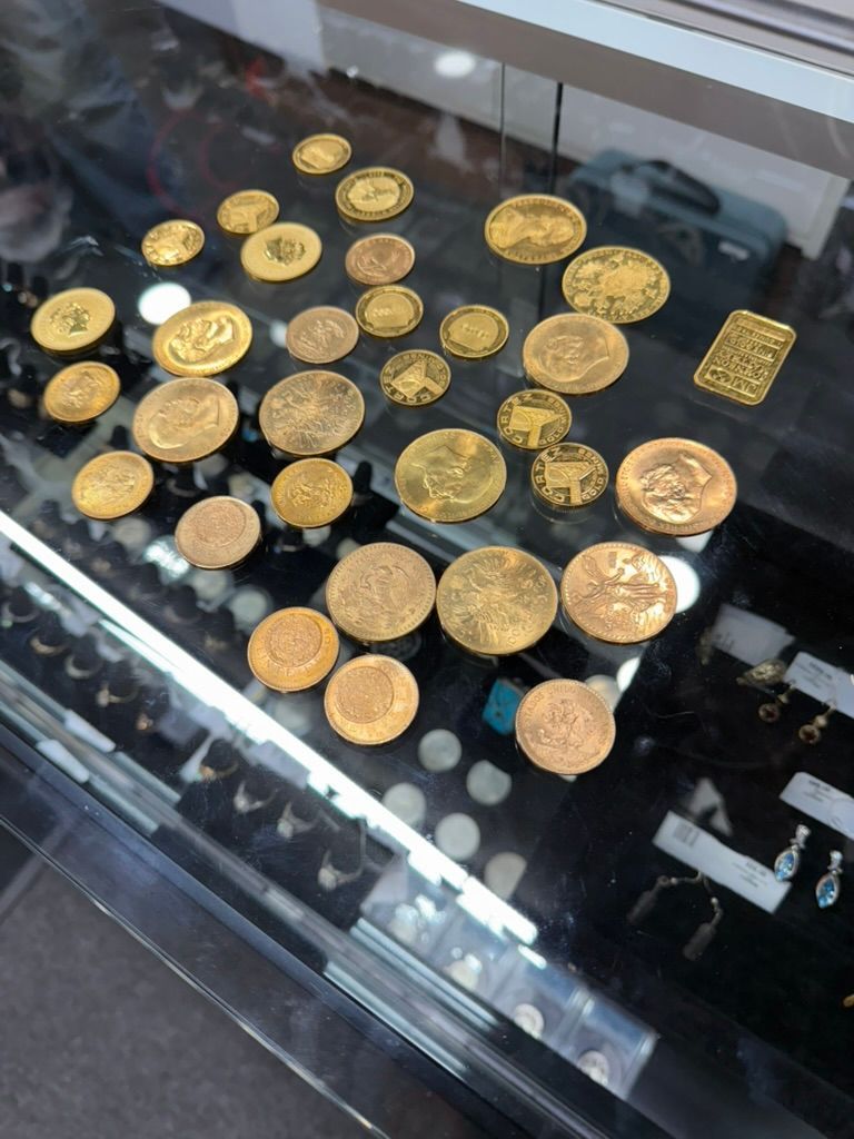 A display case containing various gold coins and a small gold bar, viewed from above.