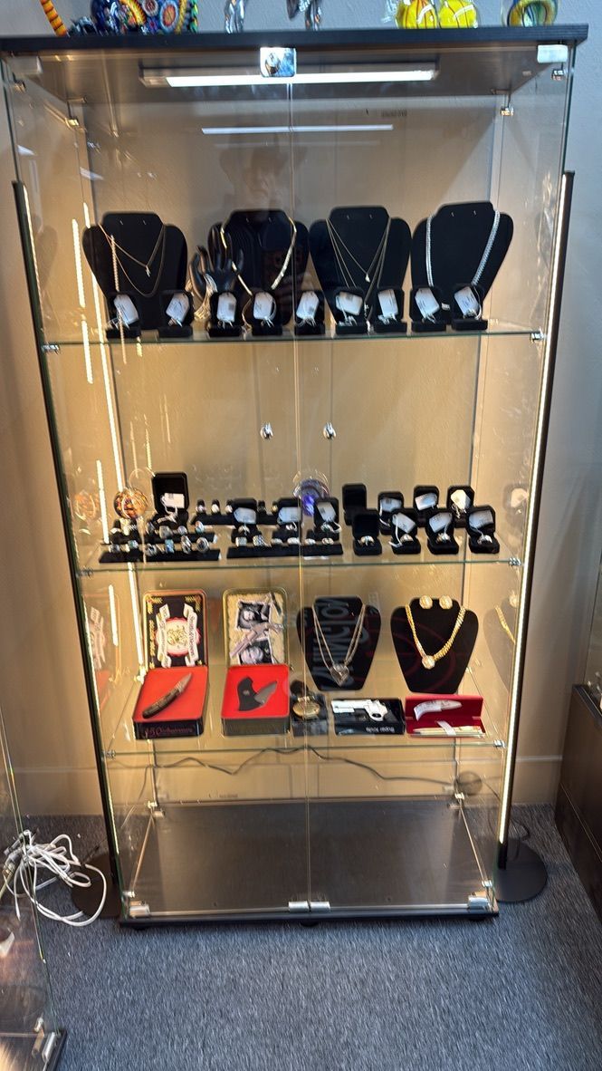 A glass display cabinet filled with necklaces, jewelry sets, and accessories arranged on shelves against a gray background.