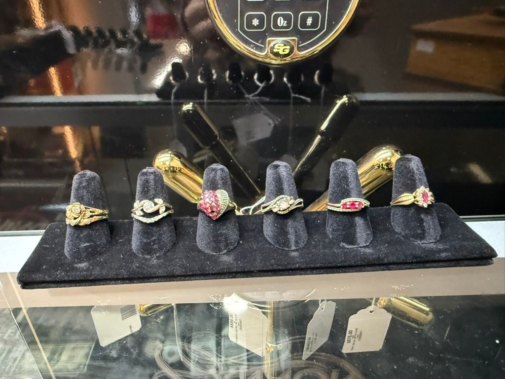 Six gold rings displayed on a black velvet stand inside a glass jewelry case.