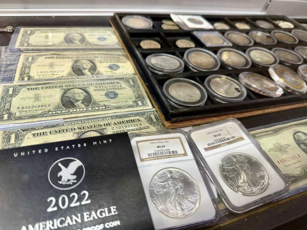 A collection of paper currency, silver coins in protective cases, and a 2022 American Eagle coin box displayed on a surface.