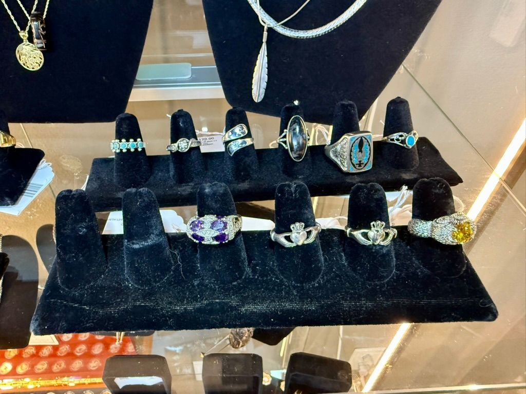 Two rows of assorted rings displayed on black velvet stands inside a glass jewelry store case.