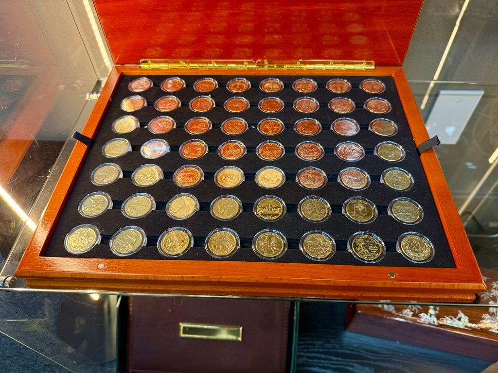 A wooden display case containing a collection of various metal coins arranged in rows on a black velvet-lined tray.