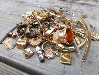 A pile of miscellaneous gold jewelry, including dental crowns, a thimble, and ring fragments, resting on a wooden surface.