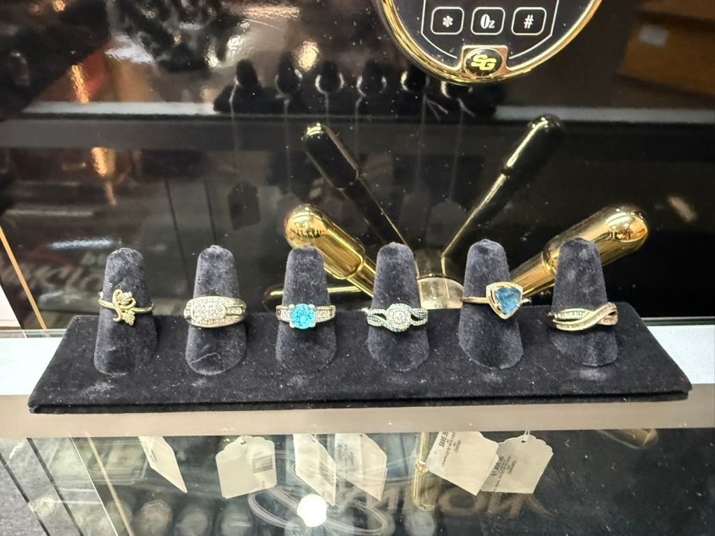 Six gold and gemstone rings displayed on velvet finger-shaped stands inside a glass display case.