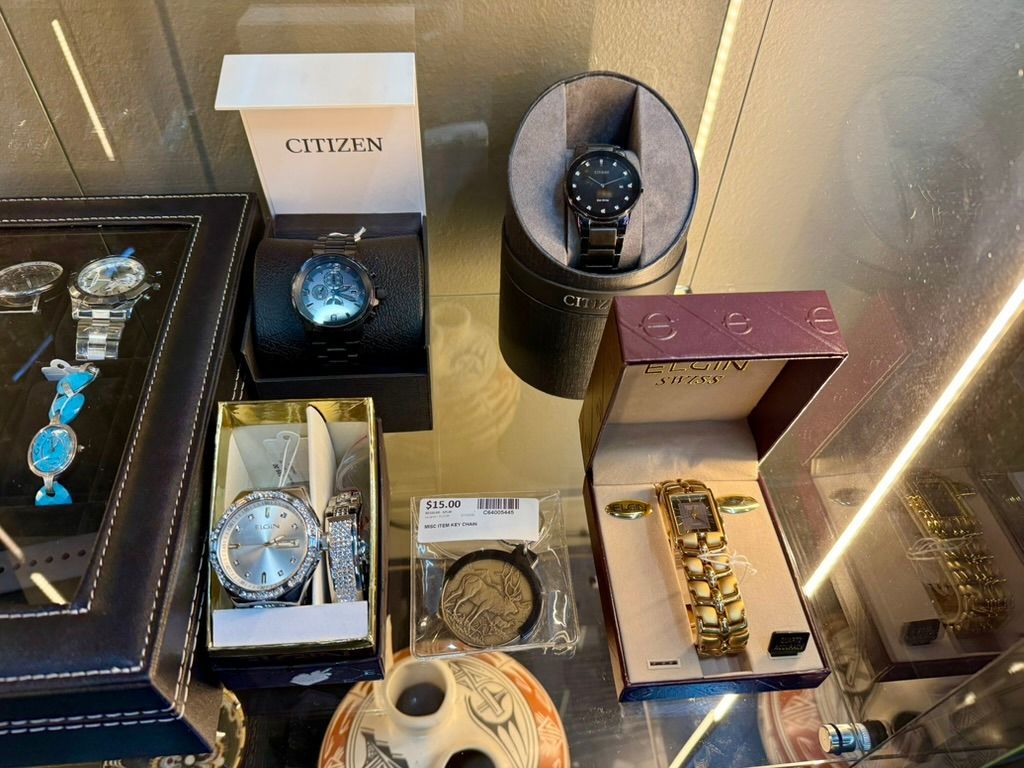 A high-angle view of watches, a pocket watch, and jewelry displayed inside a glass store display case.