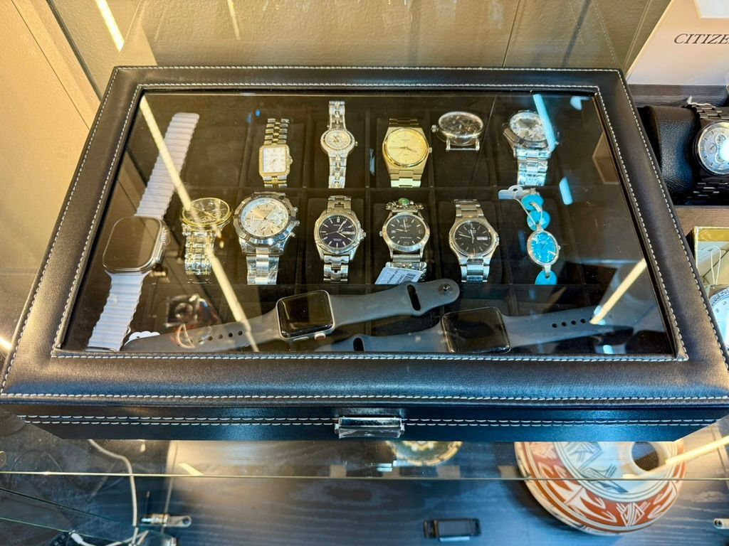 A black leather display case containing multiple wristwatches and two smartwatches arranged in rows.