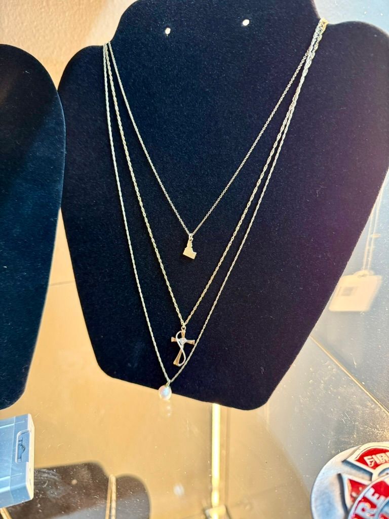 A black jewelry display bust wearing three gold necklaces with small pendants against a beige background.