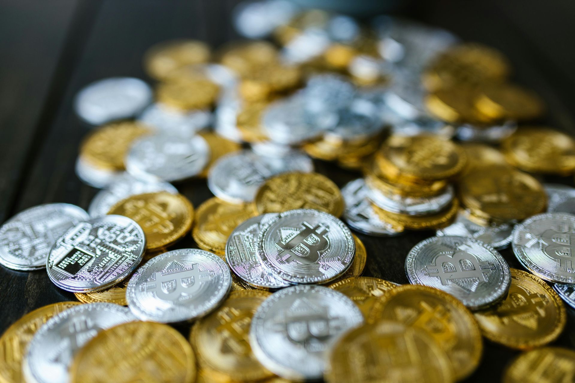 A scattered collection of gold and silver bitcoin tokens resting on a dark surface.