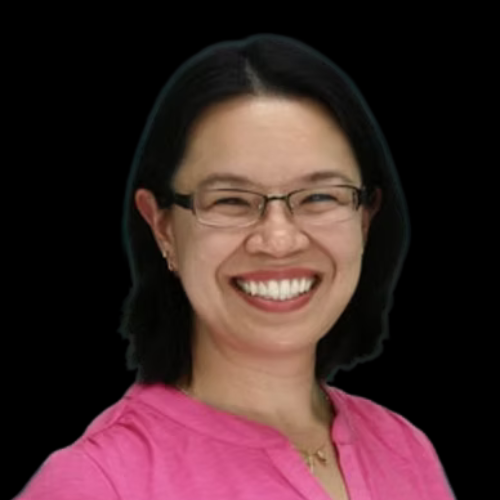 Woman with glasses smiles broadly, wearing a pink shirt, set against a black background.