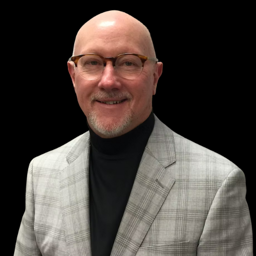 Man with glasses in a gray plaid blazer, black turtleneck, smiling in front of a black background.
