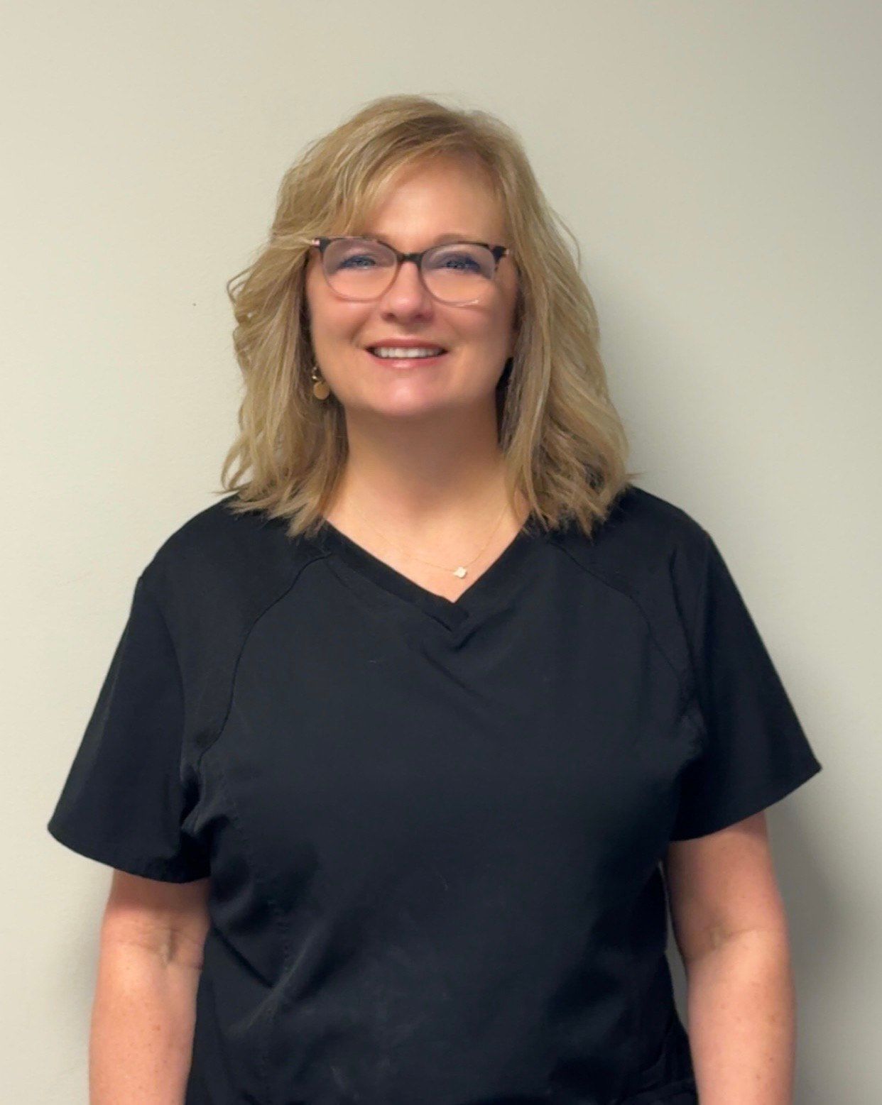 Woman with shoulder-length blonde hair smiles, wearing a polka-dot top against a black background.