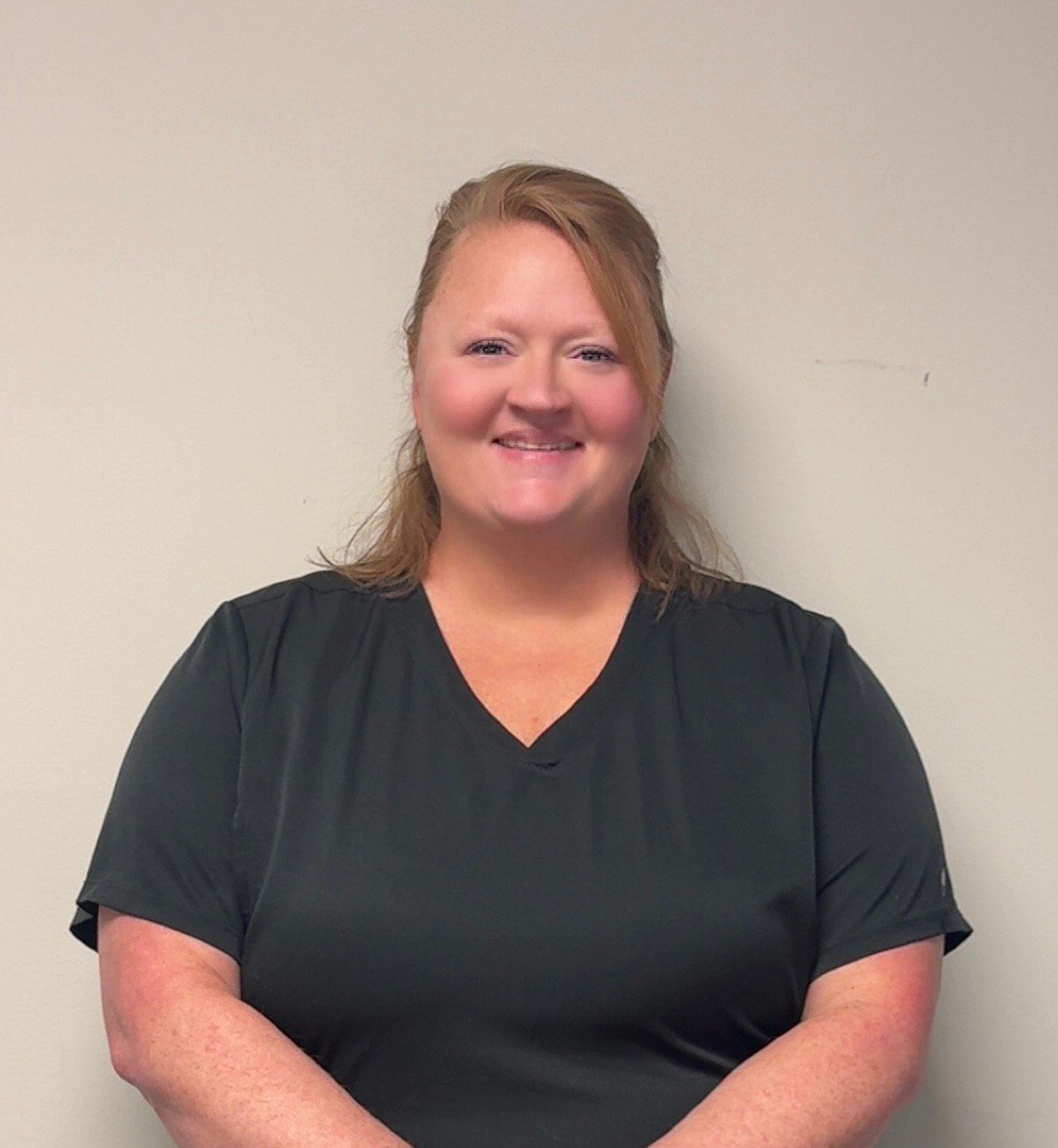 Woman with brown hair smiling, wearing a blue denim jacket over a gray sweater.