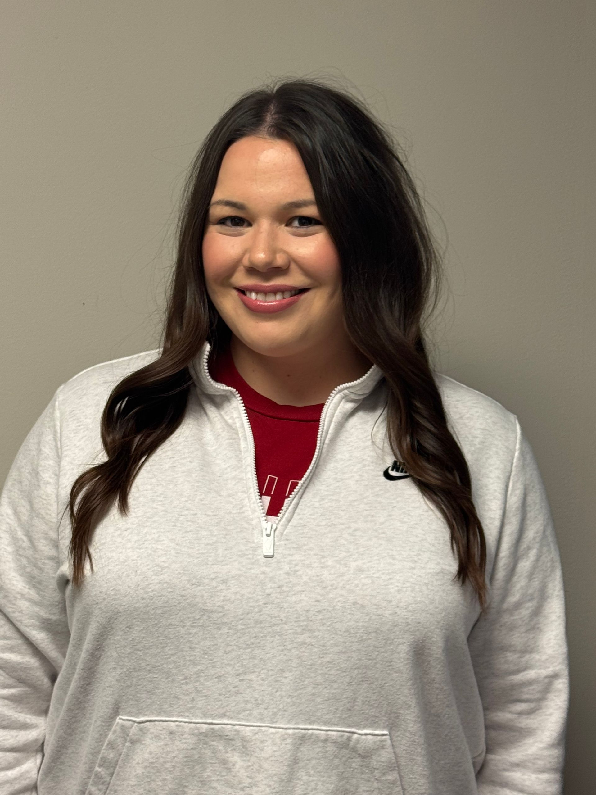 Woman with long, dark hair, wearing a gold top, smiles at the camera.