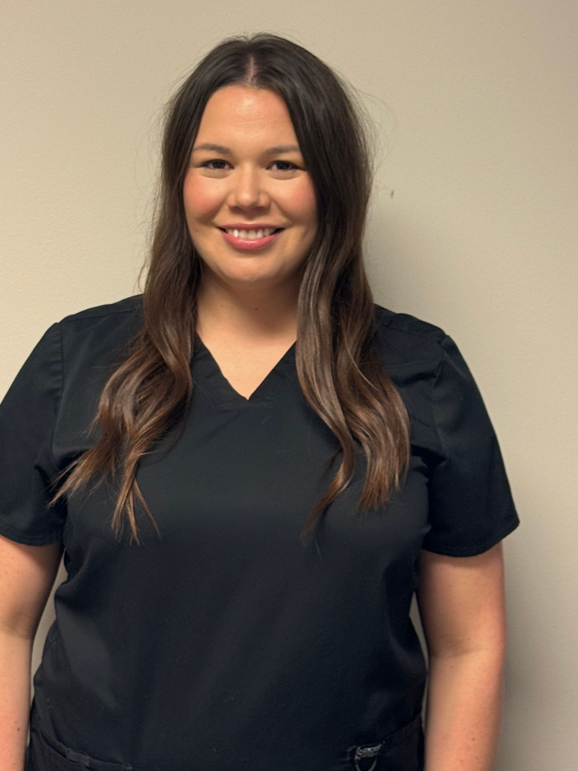 Woman with long brown hair smiles, wearing a gold top, against a black background.