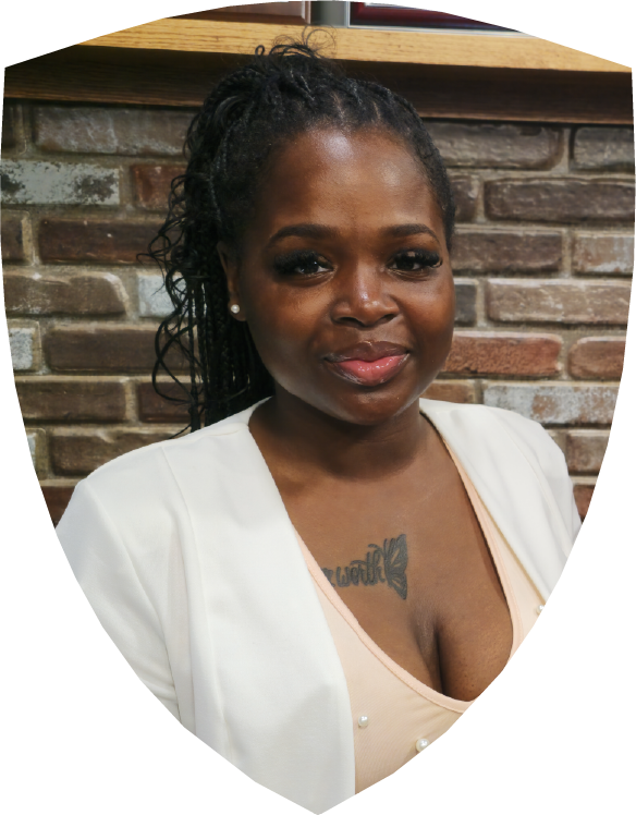 A woman in a red shirt is smiling in front of a brick wall.