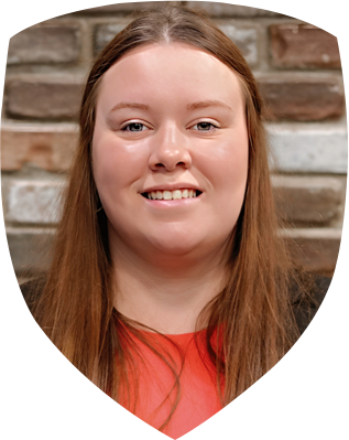 A woman in a red shirt is smiling in front of a brick wall.