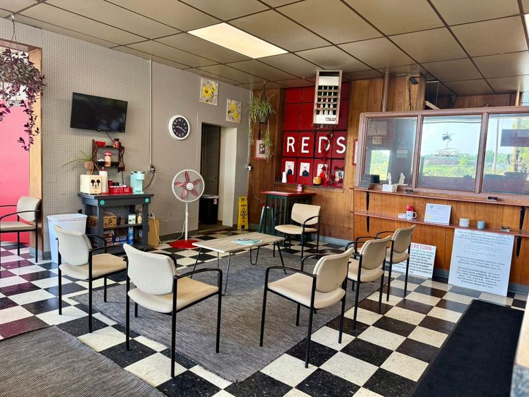 A waiting area with a black-and-white checkered floor, several chairs, a small table, a fan, and a wood-paneled counter.